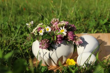 Ceramic mortar with pestle, different wildflowers and herbs on wooden board in meadow