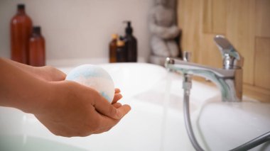 Küvetin üstünde banyo bombası tutan kadın, yakın plan. Metin için boşluk