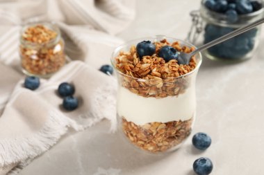 Bir bardak yoğurtlu granola ve yaban mersinli gri mermer masa, yakın plan.