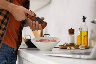 Adam mutfakta dizüstü bilgisayarla yemek kursunu izlerken yemek hazırlıyor.