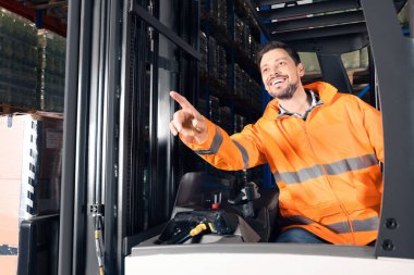 Depodaki forklift kamyonunda oturan mutlu işçi.