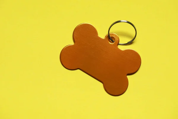 Golden pet tag in shape of bone with ring on yellow background, top view. Space for text