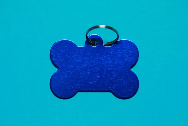 Pet tag in shape of bone with ring on light blue background, top view