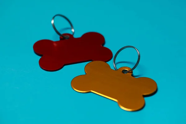 Color metal pet tags with ring on light blue background, closeup. Space for text
