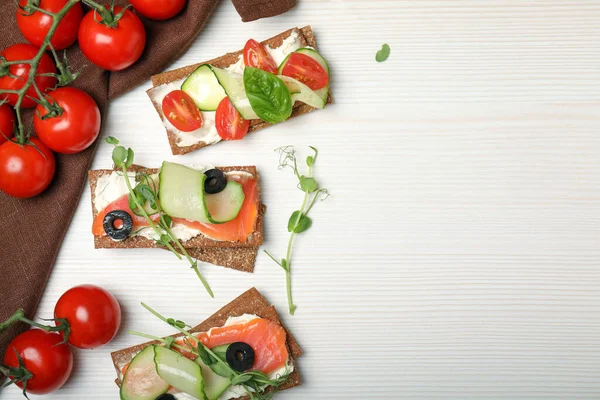 stock image Tasty rye crispbreads with salmon, cream cheese and vegetables on white wooden table, flat lay. Space for text