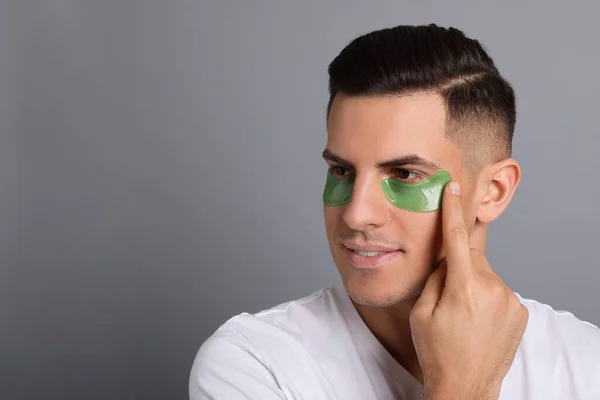 stock image Man applying green under eye patch on grey background. Space for text