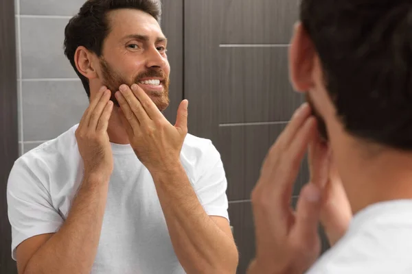 Smiling bearded man looking at mirror in bathroom
