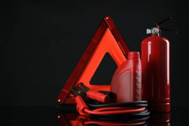 Acil durum uyarı üçgeni, kırmızı yangın söndürücü, akü takviye kabloları ve siyah arka planda motor yağı, mesaj için yer. Araba güvenliği
