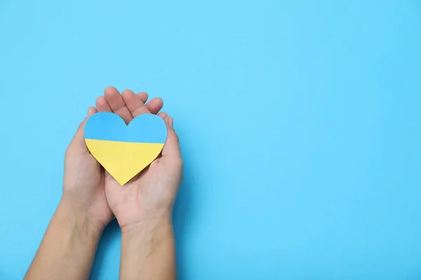stock image Woman holding paper heart in colors of Ukrainian flag on light blue background, top view. Space for text
