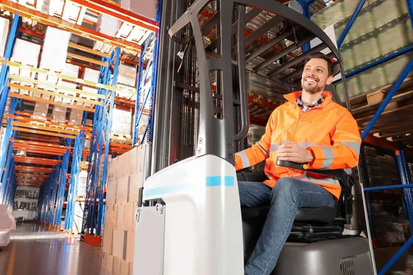 Happy worker sitting in forklift truck at warehouse
