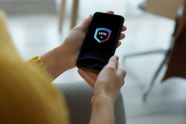 Akıllı telefonu kullanan bir kadın kapalı alanda VPN 'i açmış, yakın plan.