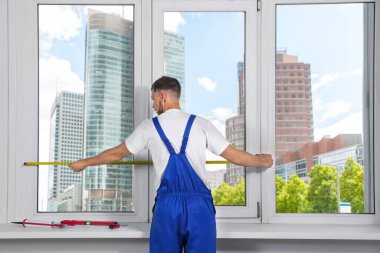 Worker measuring plastic window indoors, back view. Installation process