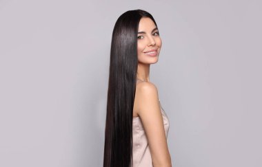 Açık gri arka planda sağlıklı, güçlü saçları olan güzel bir genç kadının portresi.