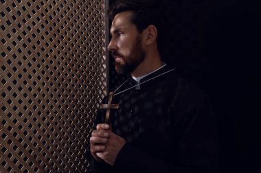 Günah çıkarma kabininde haç tutan cüppeli Katolik rahip, mesaj için yer var.