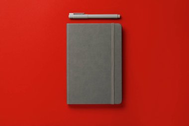 Kırmızı arka planda gri defter ve kalem düz konum