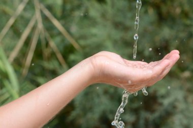 Pouring water into kid`s hand outdoors, closeup