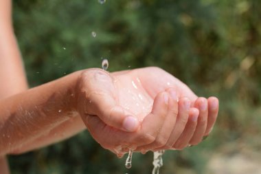 Pouring water into kid`s hands outdoors, closeup