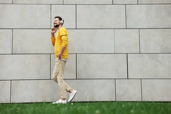 Όμορφος Άντρας Ακουστικά Που Περπατάει Κοντά Γκρίζο Πέτρινο Τοίχο Εξωτερικούς — Φωτογραφία Αρχείου