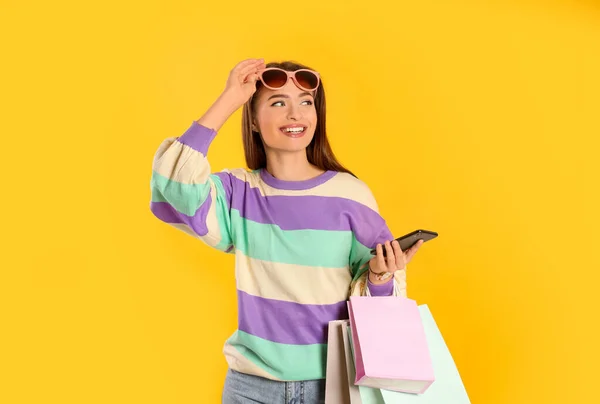 Ευτυχισμένη Νεαρή Γυναίκα Τσάντες Για Ψώνια Και Smartphone Κίτρινο Φόντο — Φωτογραφία Αρχείου