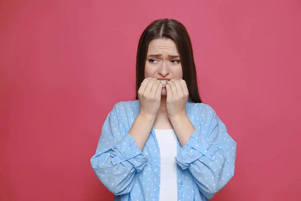 Young woman biting her nails on pink background