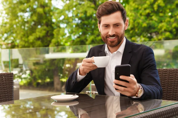 一个英俊的留着胡子的男人 在咖啡店的桌子旁 拿着一杯饮料和智能手机 — 图库照片
