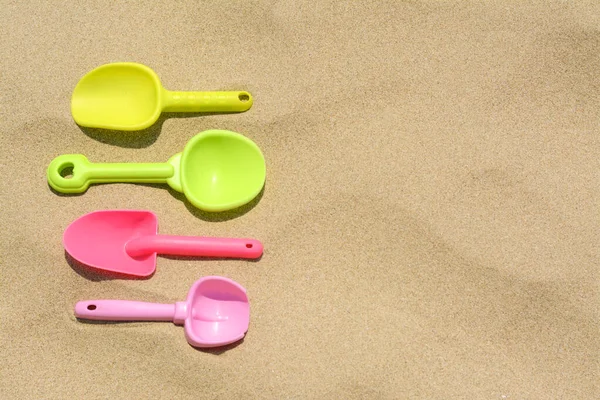 stock image Colorful plastic shovels on sand, space for text. Beach toys