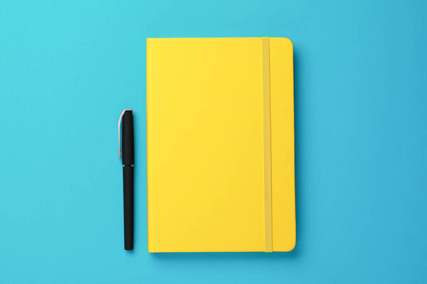Yellow notebook and pen on turquoise background, flat lay
