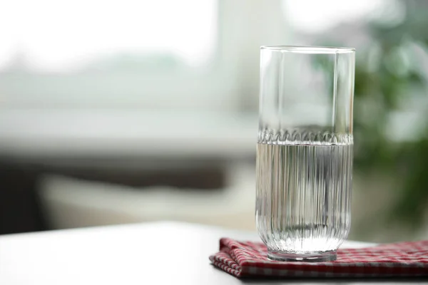 stock image Glass of pure water on light table against blurred background, space for text