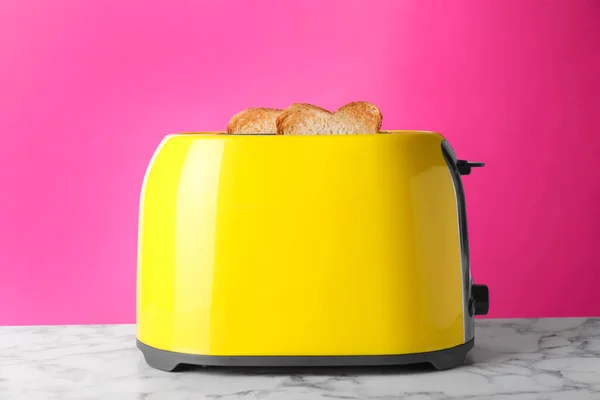 粉红背景白色大理石桌子上烤面包的黄色烤面包机 — 图库照片