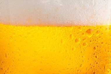 Glass of tasty cold beer with foam and condensation drops as background, closeup