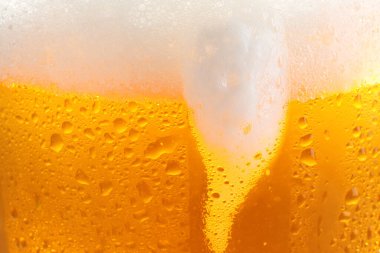 Glass of tasty cold beer with foam and condensation drops as background, closeup