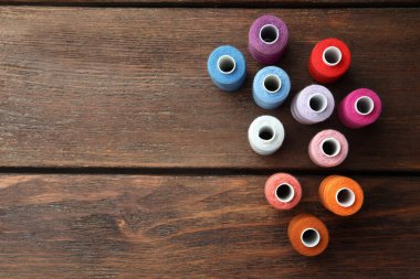 Ahşap masanın üzerine renkli dikiş iplikleri dizilmiş, düz bir şekilde. Metin için boşluk