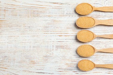 Kahverengi granüle şekerli kaşıklar açık ahşap masada, düz yatıyordu. Metin için boşluk