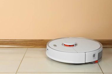 Beyaz fayanslı zeminde bej duvarın yanında robotik süpürge, metin için boşluk