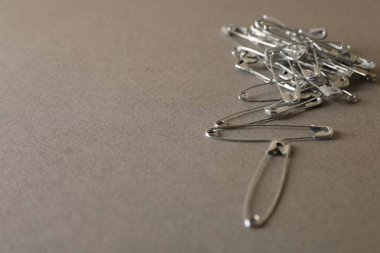 Safety pins on grey textured background, closeup. Space for text clipart