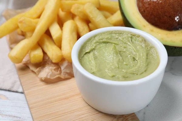 Serving board with french fries, guacamole dip and avocado on white wooden table, closeup