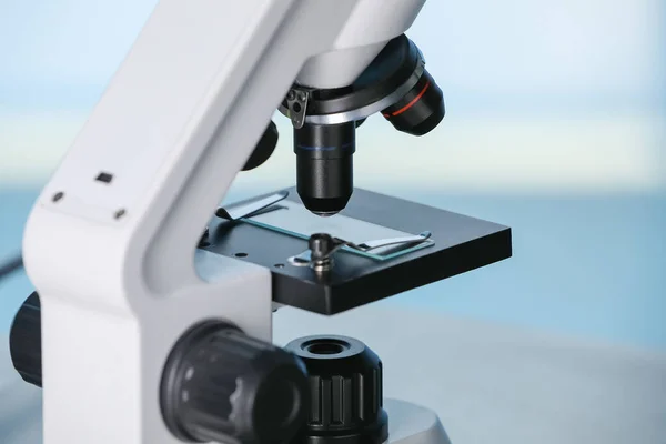 Modern microscope on light blue background, closeup. Medical equipment