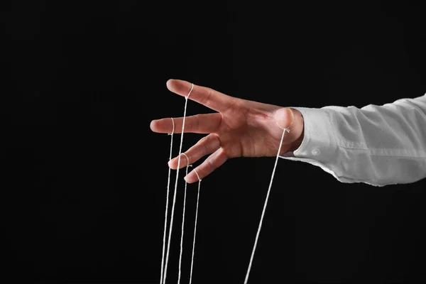 stock image Man pulling strings of puppet on black background, closeup. Space for text