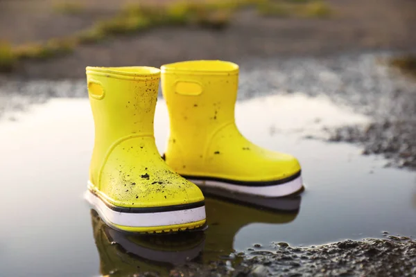 Yellow rubber boots in puddle outdoors. Autumn walk