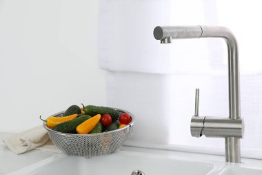 Su musluğu olan modern lavabo ve mutfak penceresinin yanında taze sebzeler.
