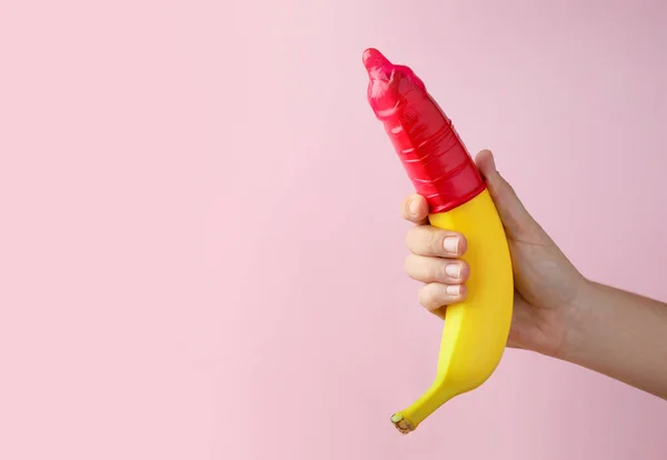 ピンクの背景 クローズアップ テキストのためのスペースにコンドームでバナナを保持する女性 安全なセックスの概念 — ストック写真