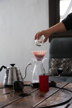 Barista kafedeki ahşap masada kahve ve damlatıcıyla sürahiye koyuyor, yakın plan.