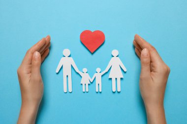 Kağıt aile figürlerini koruyan bir kadın ve açık mavi arka planda kırmızı kalp. Sigorta konsepti