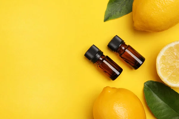 柑橘類のエッセンシャルオイルのボトル 黄色の背景に新鮮なレモンと葉 フラットレイアウト テキストのスペース — ストック写真