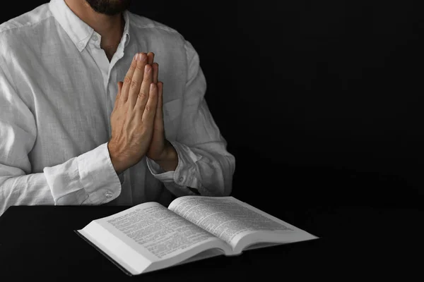 Man with Bible praying at black table, closeup