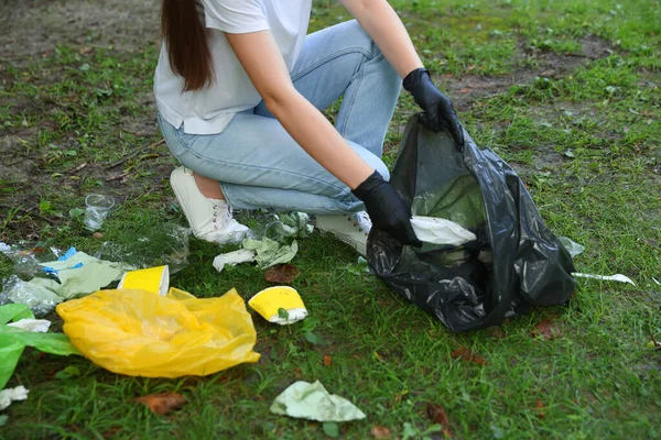 Woman with plastic bag collecting garbage on green grass, closeup