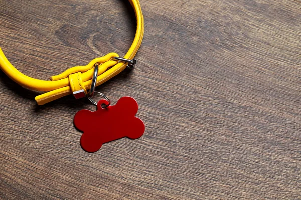 Yellow leather dog collar with red tag in shape of bone on wooden table, top view. Space for text