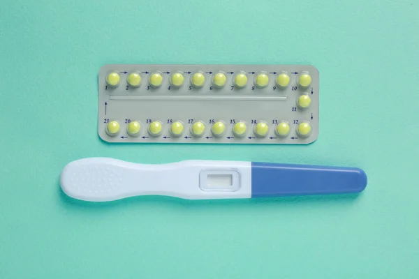 Birth control pills and pregnancy test on light blue background, top view