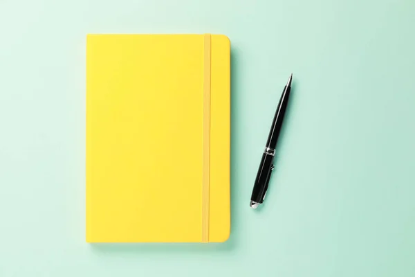 蓝绿色背景的黄色笔记本和钢笔 — 图库照片