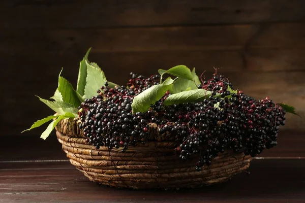 Stock image Ripe elderberries with green leaves in wicker basket on wooden table